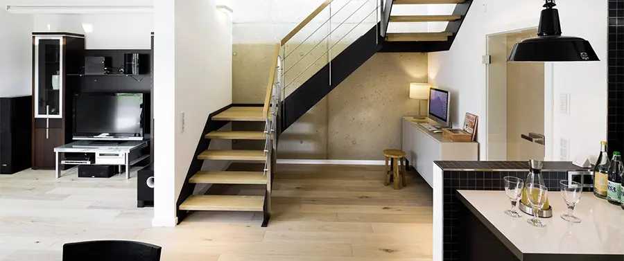 Eine moderne Kücheneinrichtung mit schwarzen Arbeitsplatten, einer Treppe (Treppenbau) mit Holzstufen und Metallgeländern sowie einem kompakten Büroraum unter der Treppe.