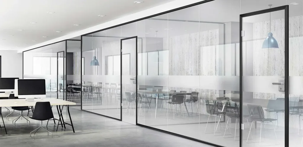 Ein moderner Büroraum mit Glasanlagen-Wänden, die transparente Trennwände zwischen einem Konferenzraum und Arbeitsbereichen bilden und mit eleganten Tischen und Stühlen ausgestattet sind. Der Raum ist gut beleuchtet und verfügt über natürliches Licht