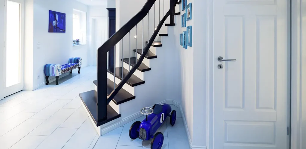 Ein moderner, hell erleuchteter Flur mit einer schwarzen Treppe, weißen Wänden und einem auf dem Boden liegenden blauen Hoverboard sorgt für einzigartige Treppeninspirationen.