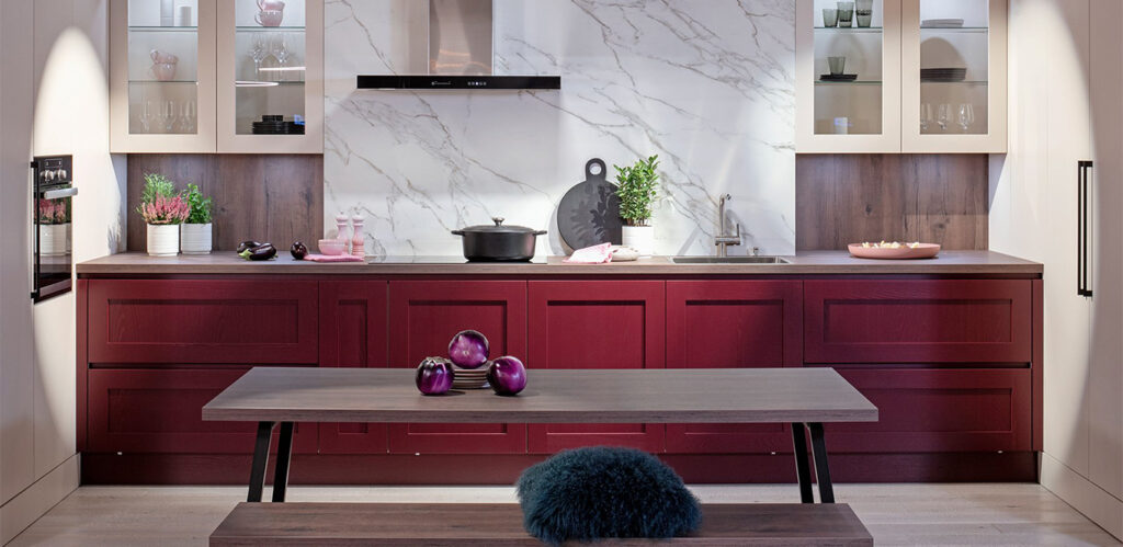 Eine moderne Küche mit burgunderroten Schränken, weißer Marmorrückwand und einem zentralen Holztisch mit violetten Akzenten für optimale Küchenpflege.