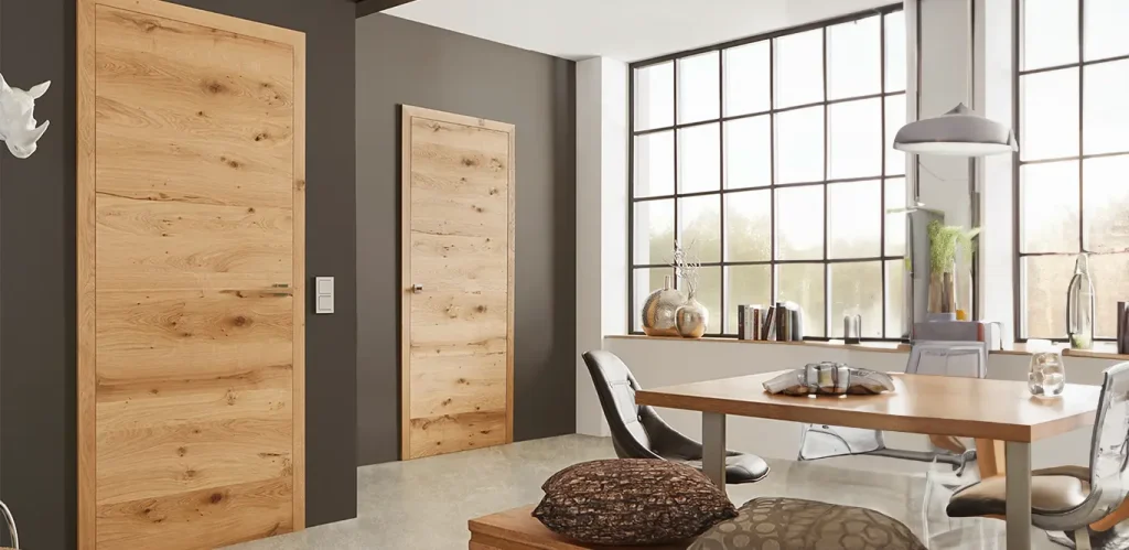 Ein modernes Esszimmer mit einem Holztisch, passenden Stühlen und zwei Echtholztüren sowie großen Fenstern, die für Tageslicht sorgen.
