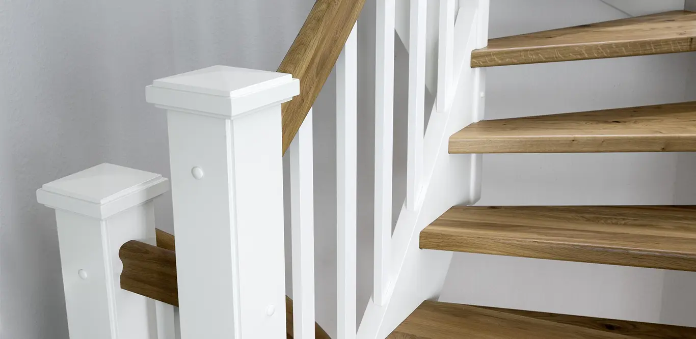 Eine moderne Treppe mit Holzstufen, weißen Handläufen und einem Geländersystem.