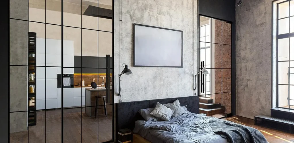 Modernes Schlafzimmer im Industriestil mit monochromatischem Farbschema, Lofttüren und einer Glaswand mit Metallrahmen, die das Schlafzimmer vom angrenzenden Raum trennt, Sichtbetonwänden und einem großen Bett mit