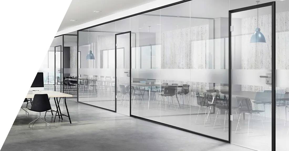 Moderne Büroräume mit Glasanlagen, einem kleinen Tisch und Stuhl im Vordergrund und einem größeren Besprechungsbereich, der durch die transparenten Trennwände sichtbar ist.