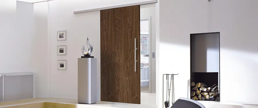 Ein moderner, minimalistischer Eingangsbereich mit einer großen Holztür mit eleganten Türgriffen, einem weißen Sockel mit einer dekorativen Vase, gerahmten Bildern an der Wand und einem Kamin mit einem Stapel Holzscheite