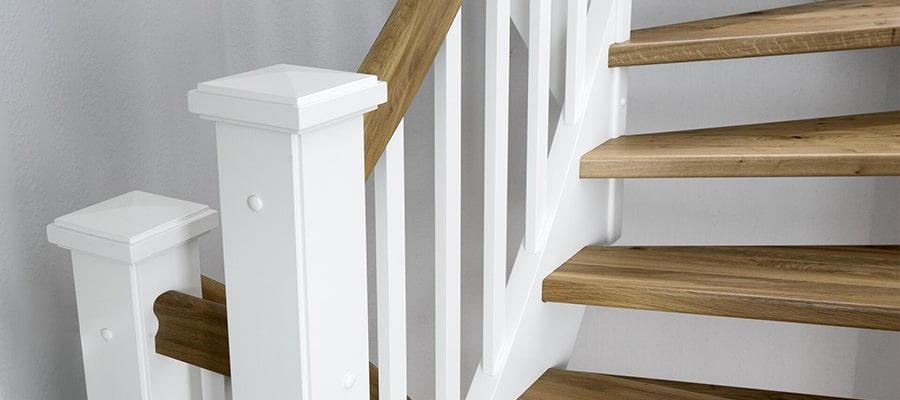Ein Teil einer Holztreppe mit weißen Treppenpfosten und Handläufen, mit Holzstufen ohne Setzstufen.