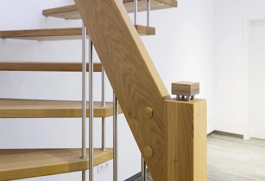 Eine moderne Holztreppe mit Treppenpfosten aus Metall und Glaspaneelen, gelegen in einem hellen Innenraum.