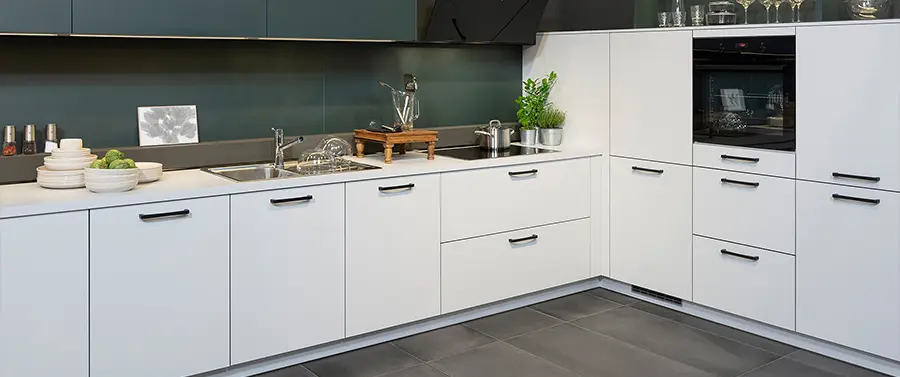 Eine moderne Design-Küche mit weißer Schrankwand, Edelstahlgeräten und einem dunklen Spritzschutz.