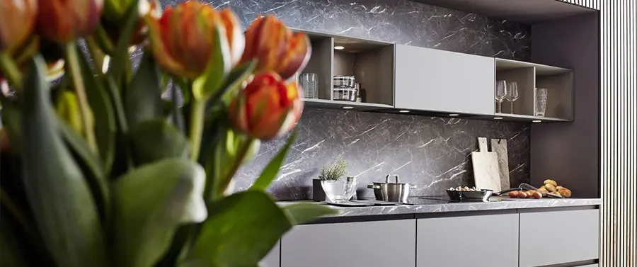 Eine moderne Küche mit Marmorrückwand, eleganten weißen Schränken und Küchengeräten aus Edelstahl, akzentuiert durch einen Strauß Tulpen im Vordergrund, präsentiert zeitgenössischen Küchenstil.