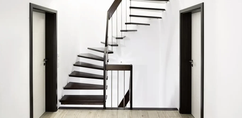 Eine moderne Treppe mit schwarzen Stufen, einem Metallgeländer und einer weißen Wand in einer minimalistischen Inneneinrichtung präsentiert verschiedene Treppenarten.