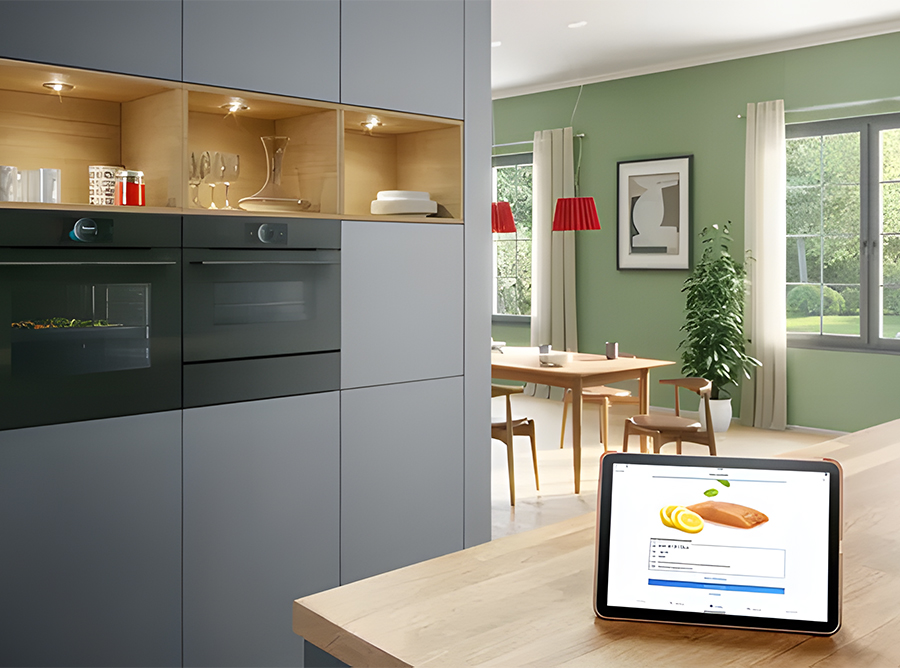 Eine moderne Küche mit grauen Schränken und Einbaugeräten sowie einem Essbereich mit einem Holztisch im Hintergrund. Auf der Küchentheke im Vordergrund steht ein Tablet, auf dem ein Rezept angezeigt wird