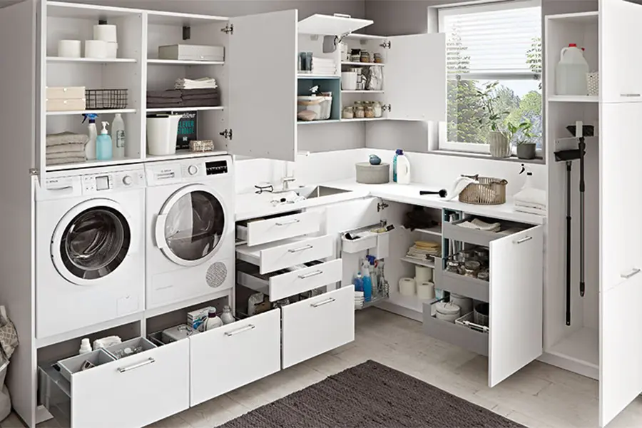 Ein moderner Hauswirtschaftsraum, ausgestattet mit einer Frontlader-Waschmaschine und einem Trockner, weißen Schränken mit mehreren Staufächern und einem Spülbecken, alles in einem sauberen und effizienten Layout organisiert.