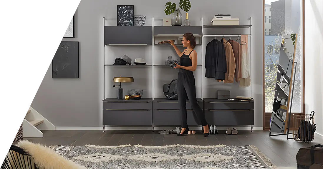 Eine Frau in einem schwarzen Outfit ordnet Gegenstände auf einem Regal in einer modernen, gut organisierten Wohnzimmereinrichtung mit einer Graustufen-Farbpalette.