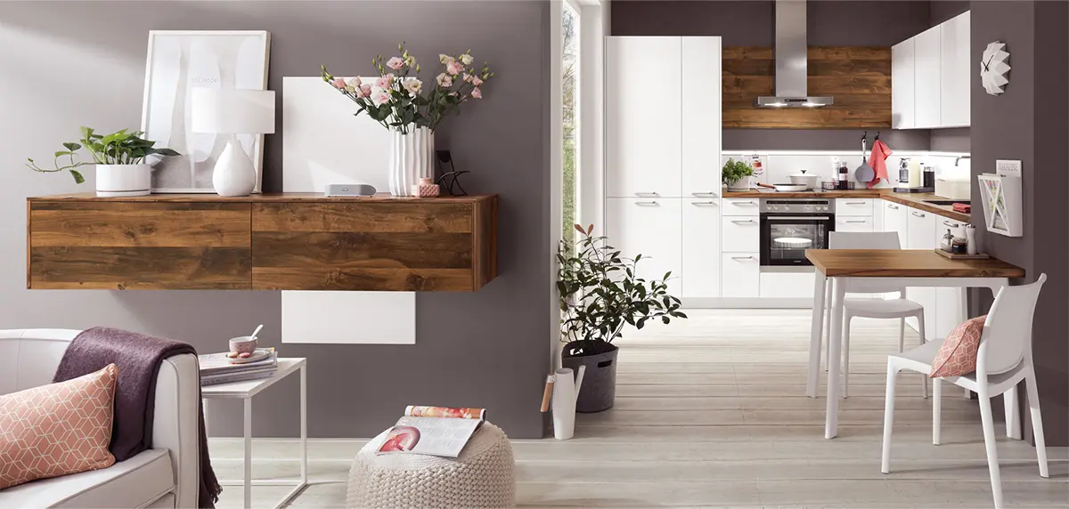 Ein moderner, übersichtlicher Küchen- und Essbereich mit Holzakzenten und hellen Wänden, einem schwebenden Regal mit Pflanzen, einem kleinen Esstisch mit Stühlen und verschiedenen klassischen Küchengeräten.