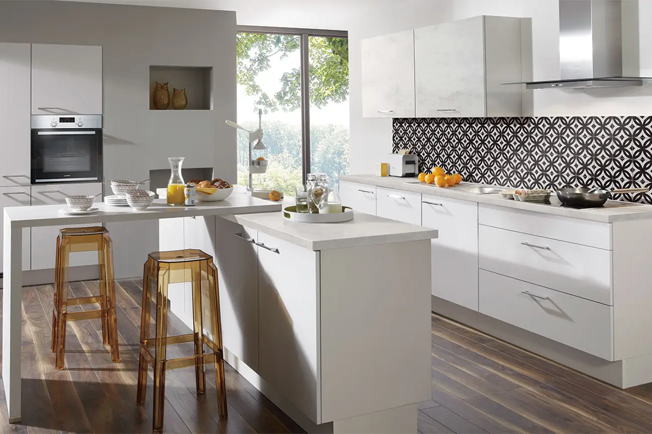 Eine moderne Kücheneinrichtung mit weißen Schränken, Geräten aus Edelstahl, einer geometrischen Rückwand und einer Frühstücksbar mit klassischen Holzhockern.