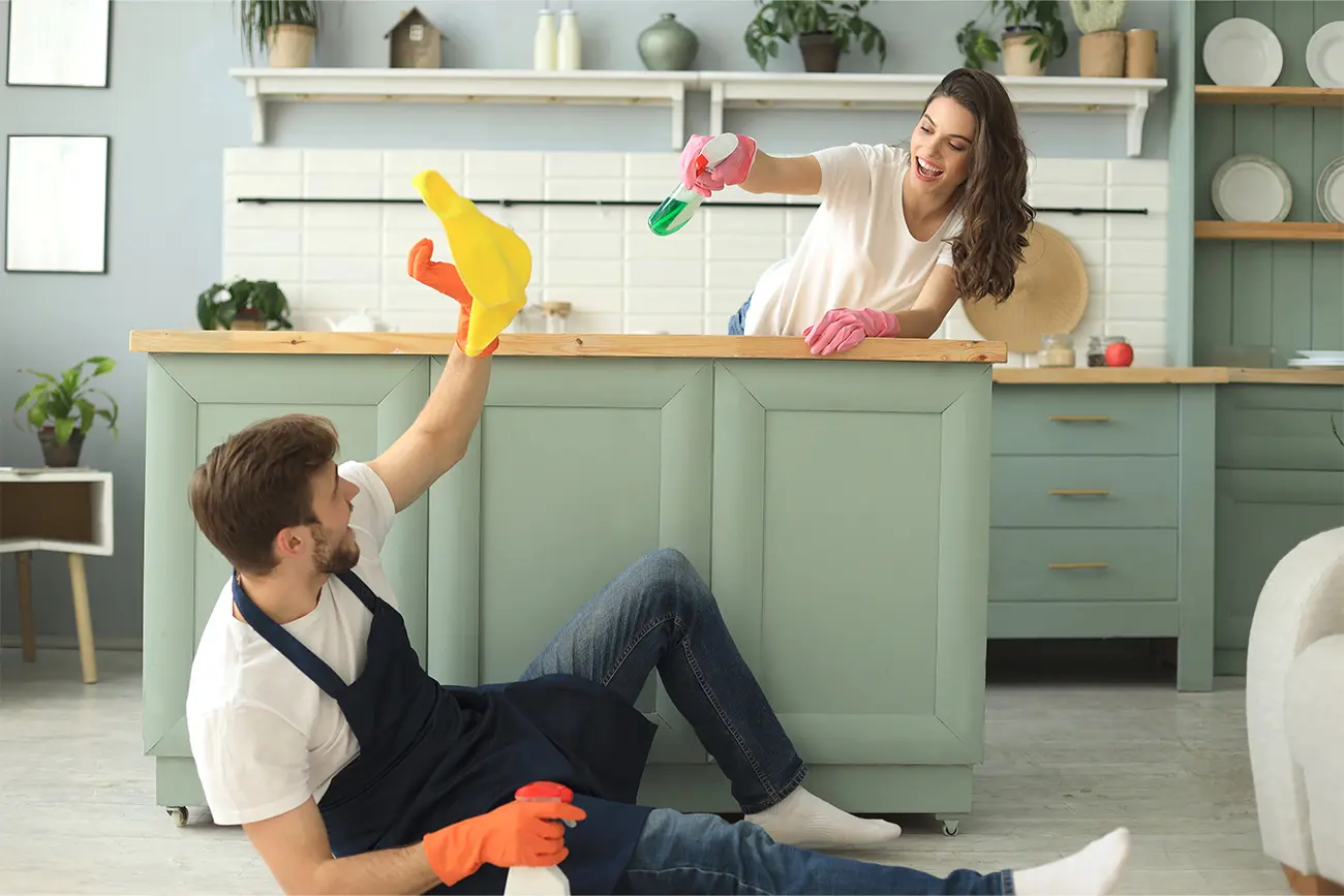Zwei Personen liefern sich im Rahmen ihrer Küchenpflege-Routine in einer Küche spielerisch einen Scheinkampf mit Reinigungsmitteln.