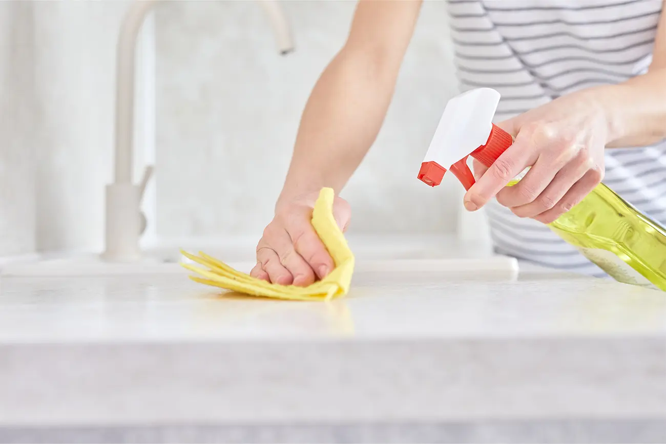 Person reinigt Küchenarbeitsplatte mit Sprühflasche und Tuch zur Küchenpflege.