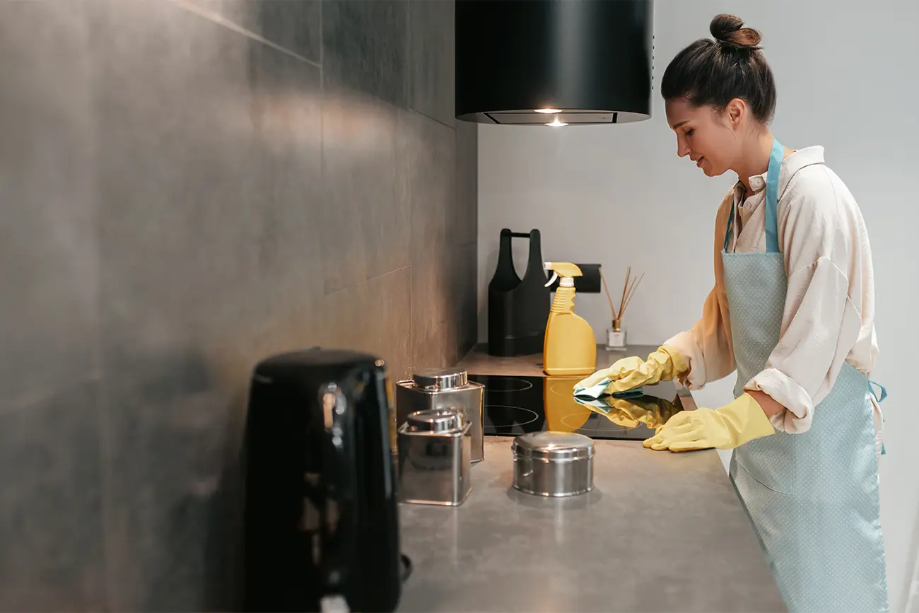 Eine Frau, die eine hellblaue Schürze und gelbe Handschuhe trägt, kümmert sich um die Küchenpflege, indem sie einen modernen Küchentres