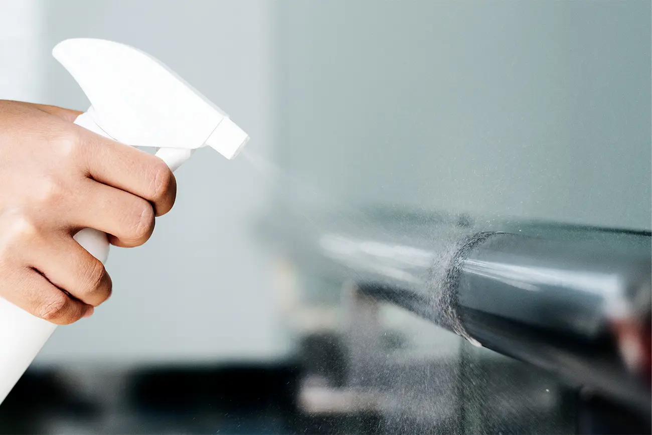 Die Hand einer Person sprüht eine Küchenpflegelösung auf eine Glasoberfläche.