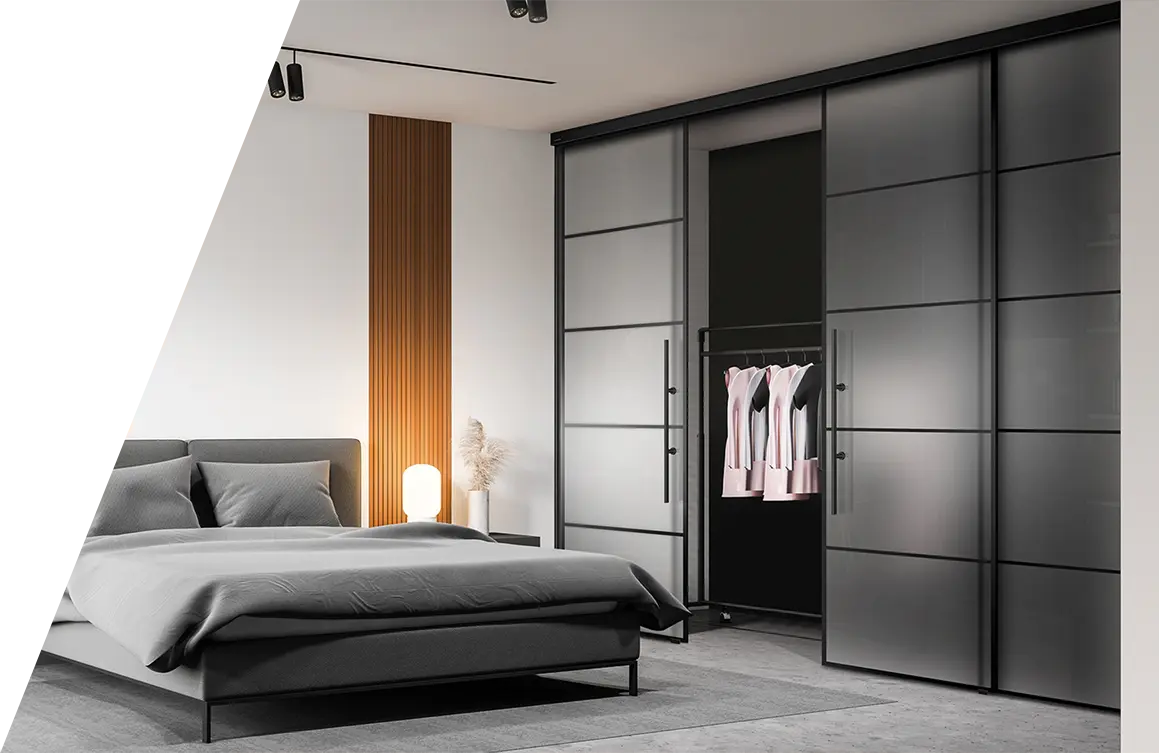 Ein modernes Schlafzimmer mit einem niedrigen Bett mit grauer Bettwäsche, einer Nachttischlampe und einem großen Kleiderschrank mit offenen Glastüren, in dem hängende Kleidung ausgestellt ist. Das Zimmer verfügt über ein minimalistisches Design mit neutralen Farbtönen