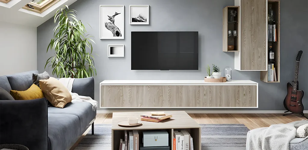 Eine moderne Wohnzimmereinrichtung mit einem grauen Sofa, einem montierten Flachbildfernseher, Holzregalen und einer Gitarre, die gegen die Wand ge