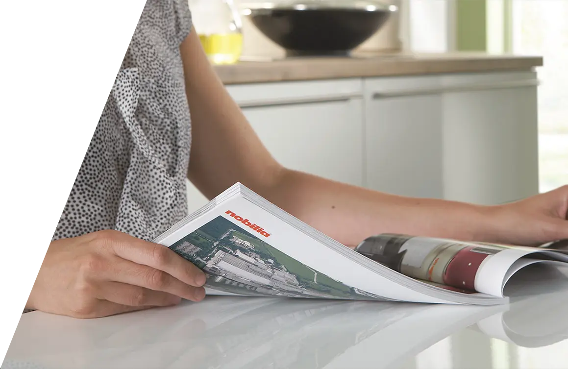 Eine Person sitzt an einer Nobilia-Küchentheke und blättert in einer Zeitschrift, auf deren Titelseite das Wort „Rezepte“ zu sehen ist.