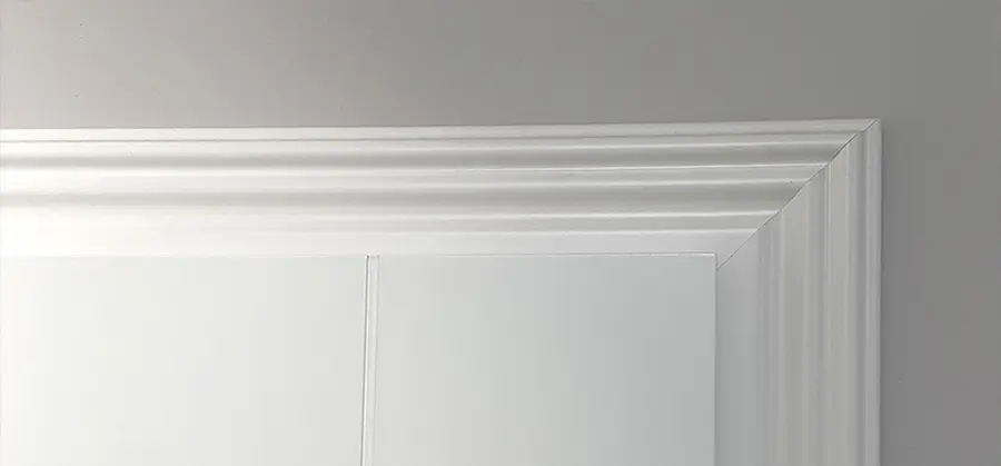 Weiße Zierleiste oben an der Wand, die an die Decke angrenzt, in einem Raum mit sanftem Grauton und eleganten Innentüren.