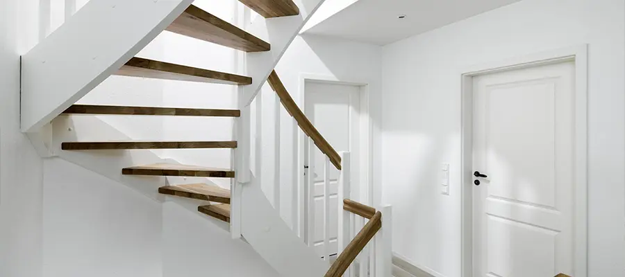 Ein modernes Interieur mit schwebenden hölzernen Wangentreppen mit weißen Wänden und zwei geschlossenen Türen.