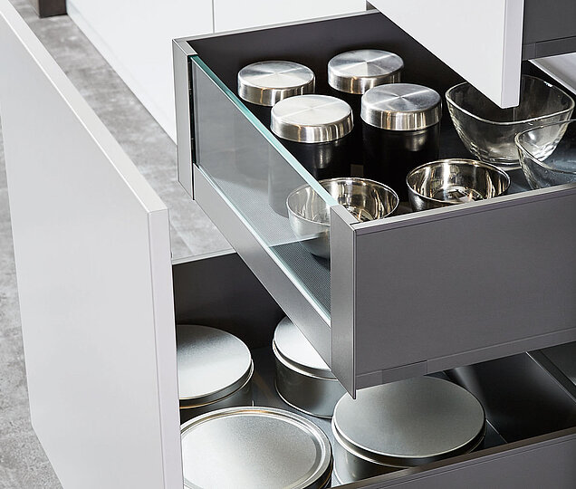 Eine moderne Möbel-Küchenschublade, die teilweise geöffnet ist und den Blick auf organisierte Fächer mit Metalldeckeln und -schalen freigibt.
