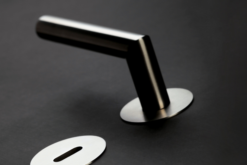 Ein moderner, minimalistischer Griffwerk-Türgriff aus Metall auf einer schwarzen Oberfläche neben einer Schlüssellochplatte.