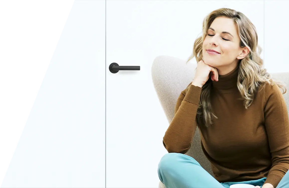 Eine Frau mit geschlossenen Augen sitzt neben einem weißen Bora-Kochfeldabzug, ihr Kinn auf ihre Hand gestützt und lächelt zufrieden. Sie trägt einen braunen Rollkragenpullover und Türkis