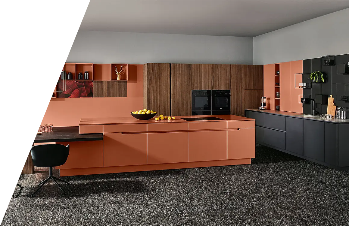 Moderne Kücheneinrichtung mit Schränken aus Holz und Orange, Geräten aus Edelstahl, darunter ein Bora-Kochfeldabzug und einem schwarzen Hocker an der Theke.