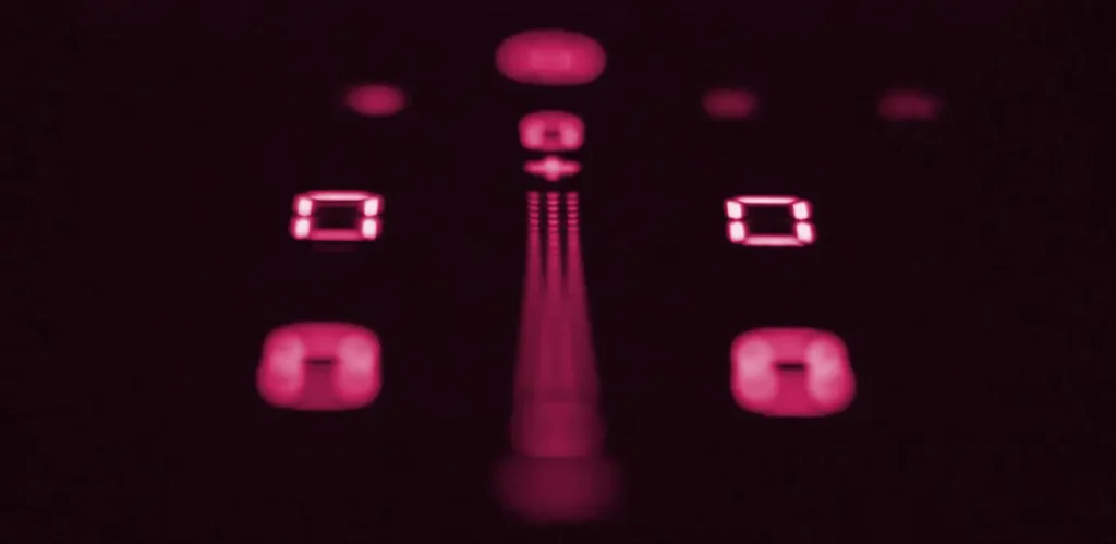 Abstrakte rote Lichter, die ein symmetrisches Muster mit einer zentralen vertikalen Linie und mehreren verschwommenen geometrischen Formen auf dunklem Hintergrund bilden, einschließlich Kochfeldabzüge-Motiven.