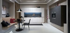 Moderner Küchen- und Essbereich mit monochromer Farbgebung, weißen Schränken, Einbaugeräten und einem kleinen runden Esstisch mit Platz für zwei Personen.