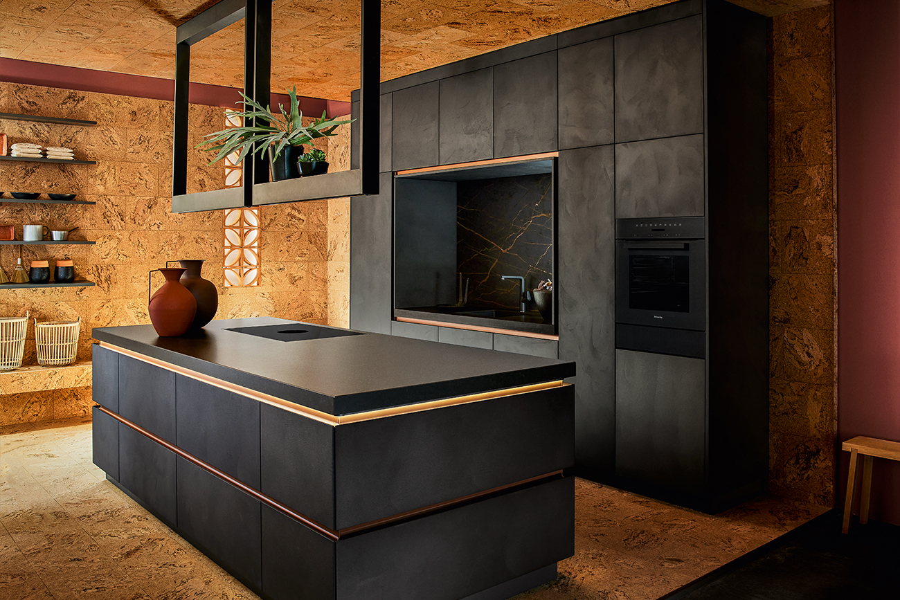 Eine moderne Designküche mit dunklen Schränken, Einbaugeräten und einer Kochinsel mit Arbeitsplattenherd vor einer erdfarbenen, strukturierten Wand.
