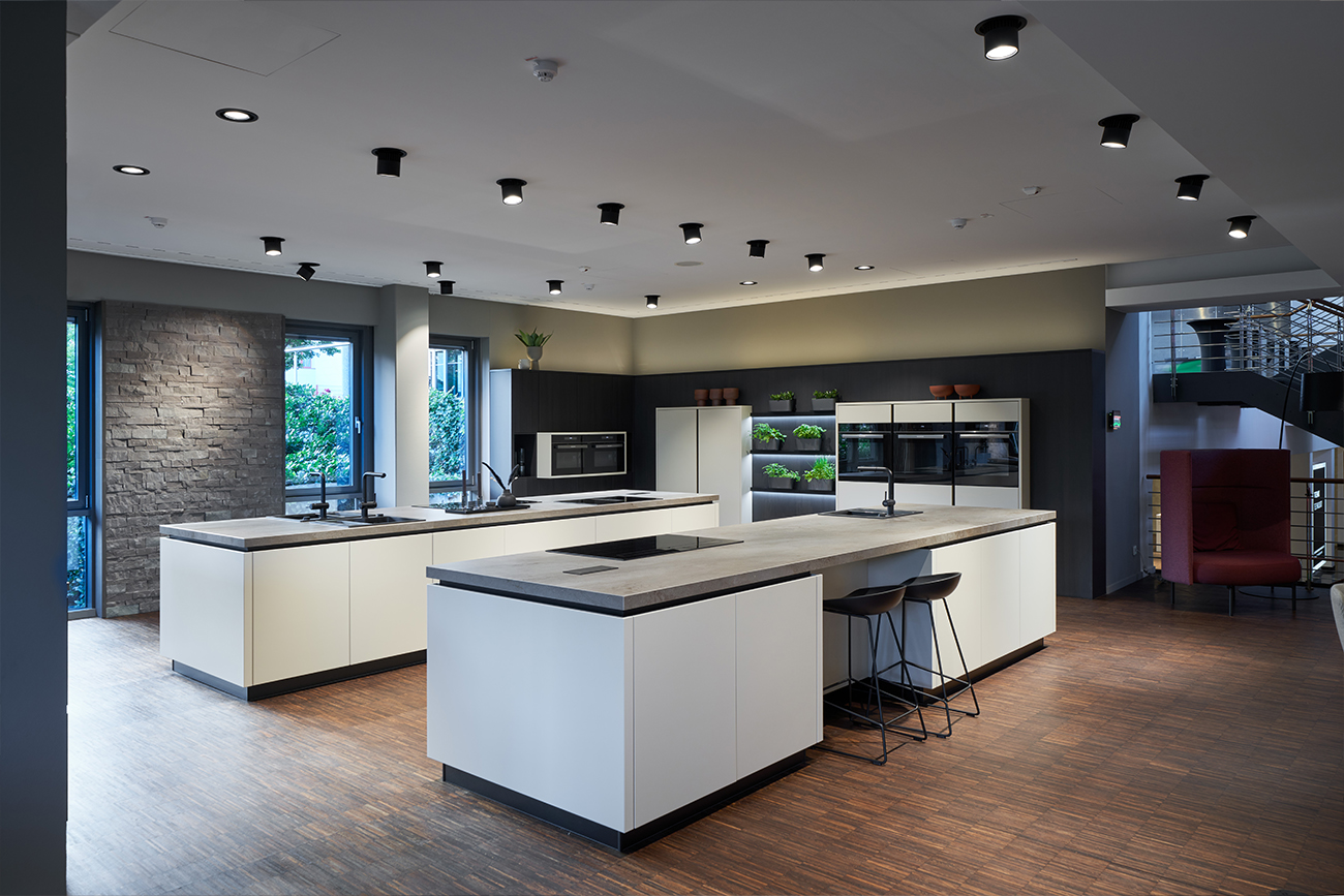 Moderne Kücheneinrichtung mit zentraler Kücheninsel, Barhockern und Einbaugeräten, dunklem Holzboden und stimmungsvoller Beleuchtung. Diese Individuelle Küche betont Einzigartigkeit und persönlichen Stil.