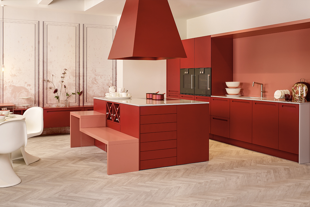 Eine moderne individuelle Küche mit roten Schränken, integrierten Geräten und einer zentralen Insel, die sich in einen Esstisch verwandelt, vor einem neutralen Boden und neutralen Wänden.
