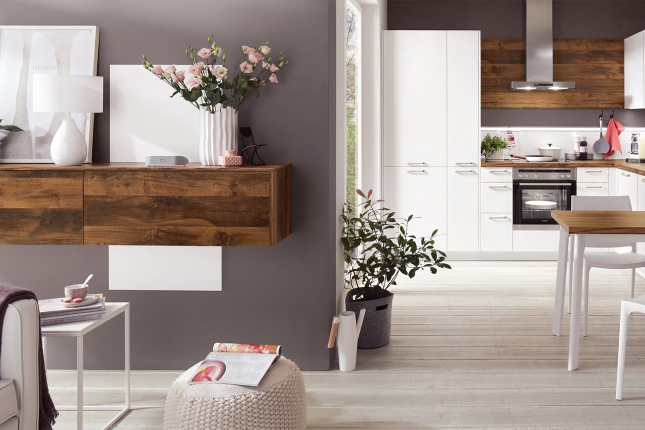 Ein modernes, aufgeräumtes Interieur mit offenem Design und einem Wohnbereich, der nahtlos mit einer klassischen Küche verbunden ist, akzentuiert durch Holzoberflächen und neutrale Farbtöne.