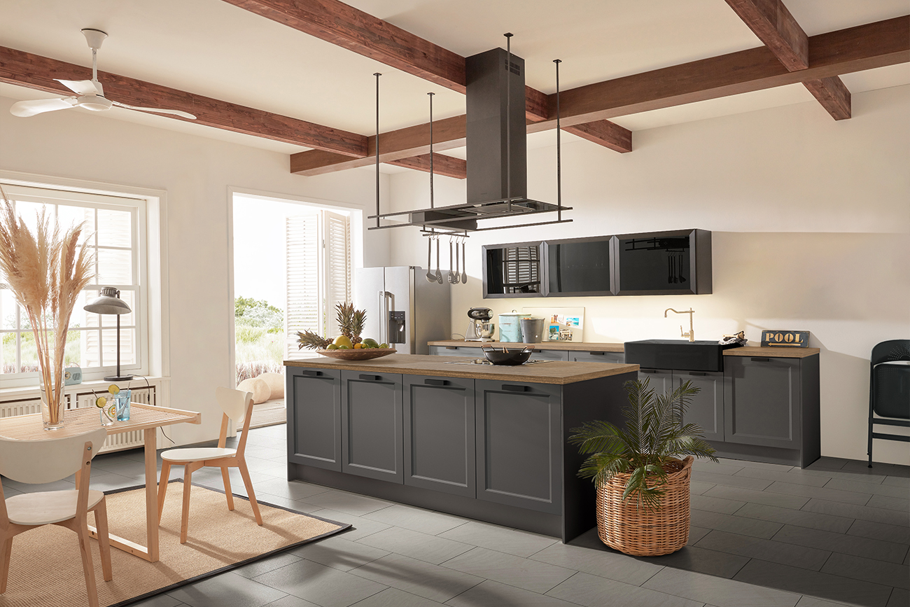 Moderne Küche mit grauen Schränken, Geräten aus Edelstahl und einer zentralen Insel unter freiliegenden Holzbalken im Landhausküchen-Stil.