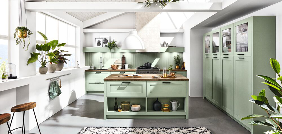 Eine moderne Küche mit salbeigrünen Schränken, Arbeitsplatten aus Holz und einer Auswahl an Zimmerpflanzen, die ein frisches und natürliches Ambiente schaffen.