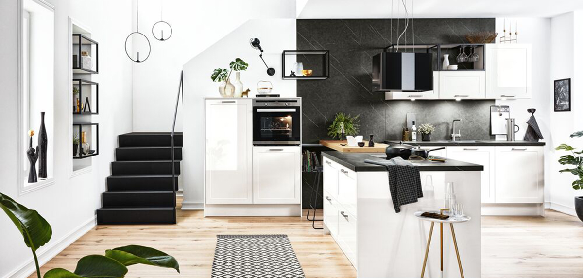 Moderne Küche mit Schwarz-Weiß-Farbschema, einer zentralen Kochinsel, Küchengeräten aus Edelstahl und einer Treppe, die zu einer oberen Ebene führt.