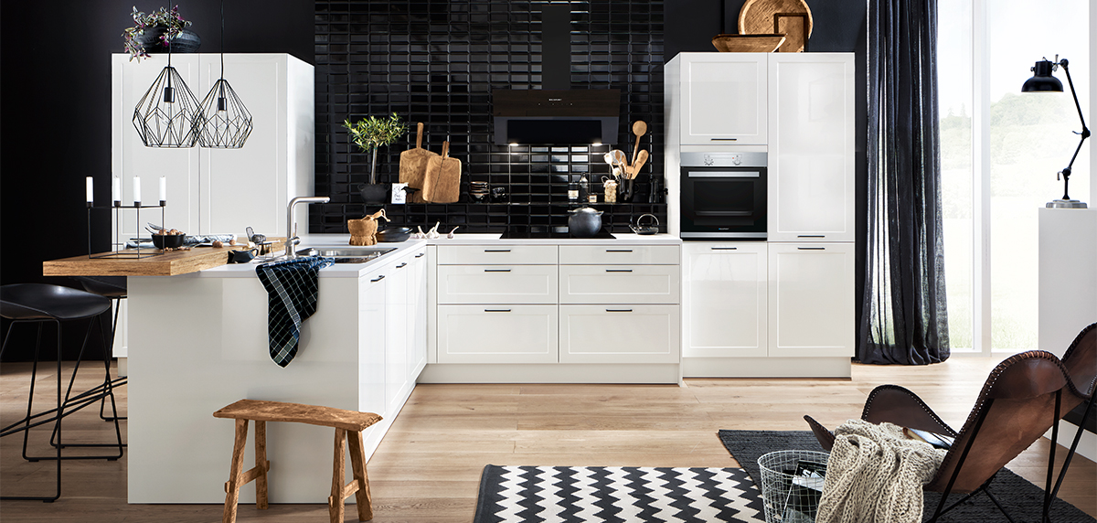 Eine moderne Küche im Landhausküchen-Stil mit weißen Schränken, schwarzen Spritzschutzfliesen und Geräten aus Edelstahl, einer zentralen Insel mit Sitzgelegenheiten und einem Boden mit Fischgrätenmuster.