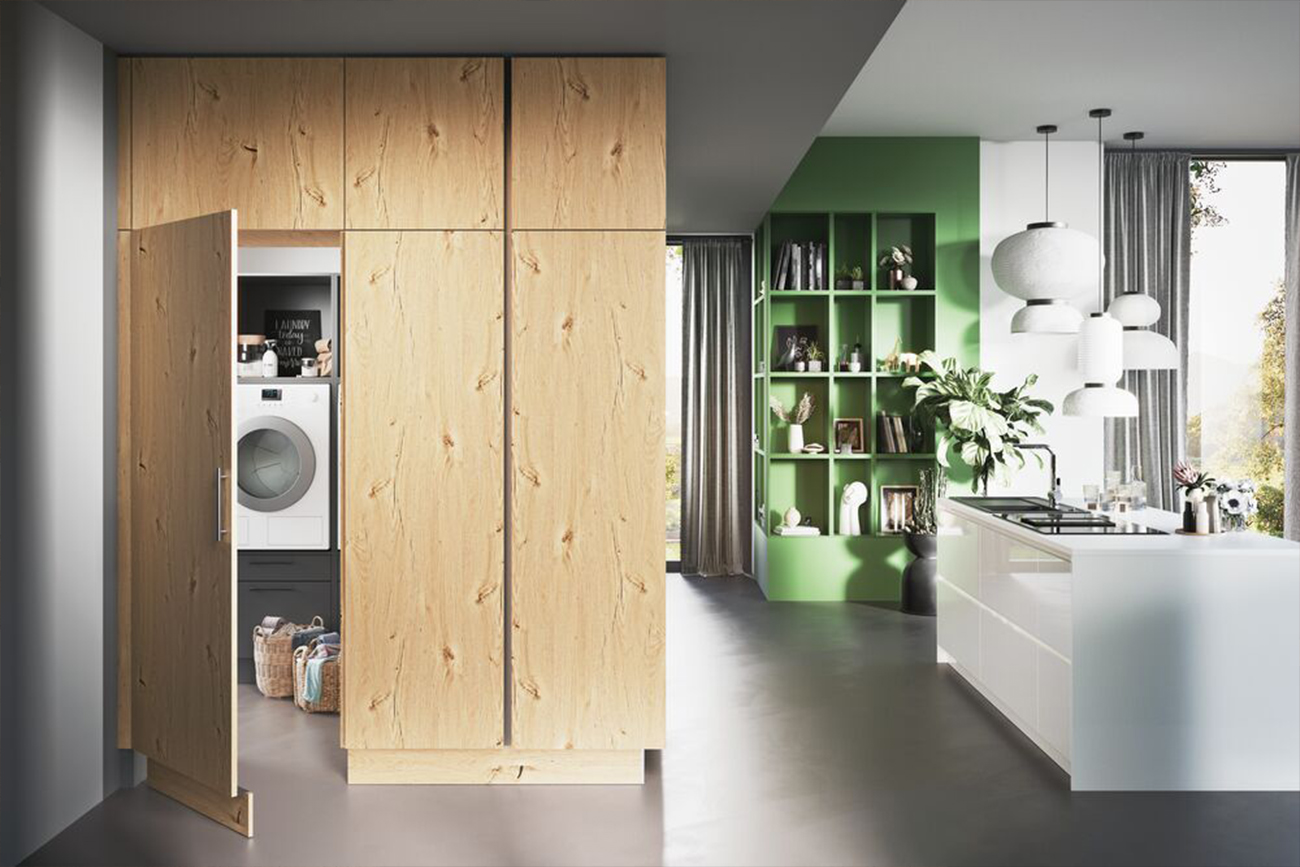 Ein modernes Bild mit geteilter Ansicht, das links eine hinter Holztüren verborgene Waschküche und rechts einen eleganten Natural Living Küchen-Bereich mit grünen Regalen und weißen Arbeitsplatten zeigt.
